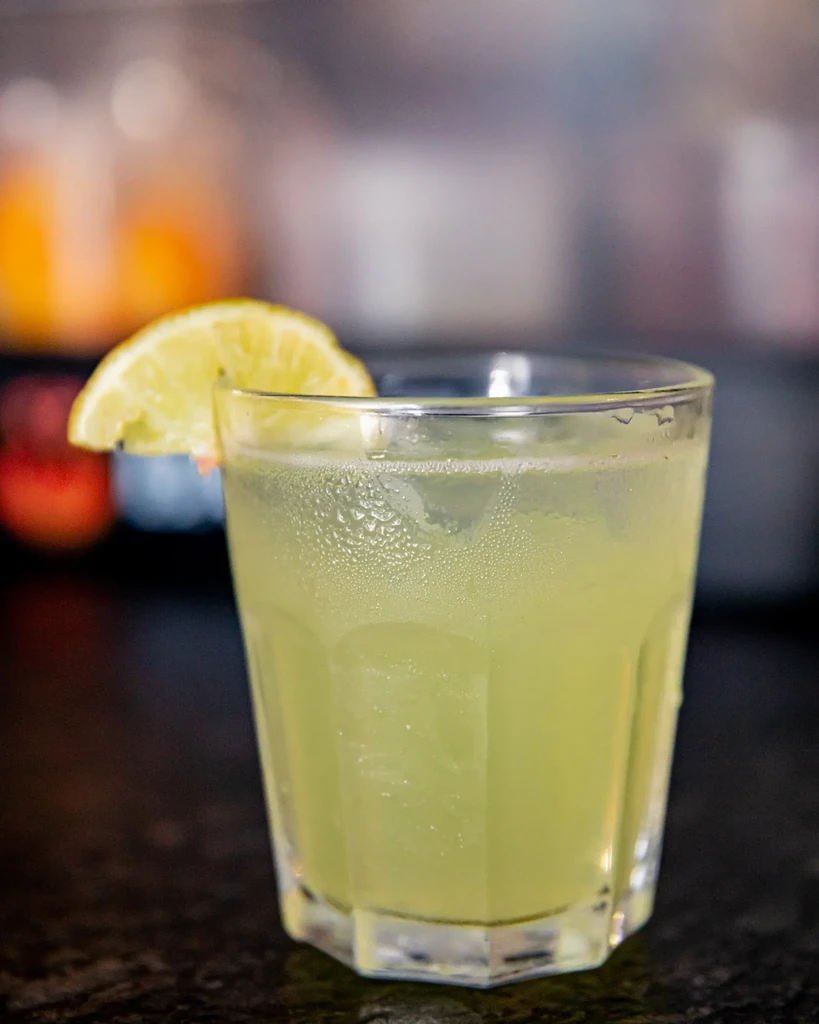 A sweating glass of limeade with a lime wedge on a dark surface.