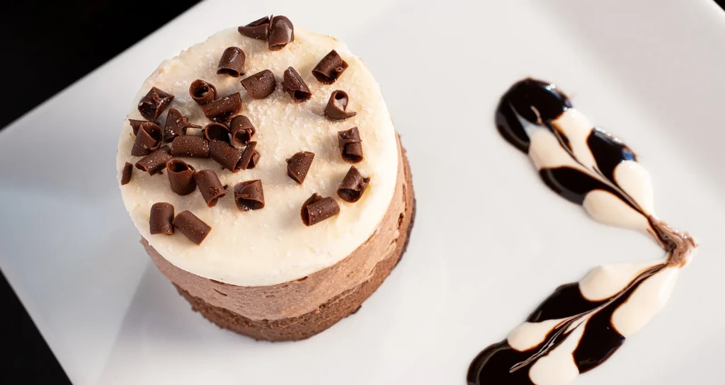 Chocolate mousse cake with white frosting and chocolate curls on a white plate.