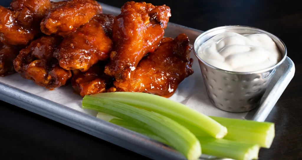 Glazed chicken wings, celery sticks, and a small cup of sauce.