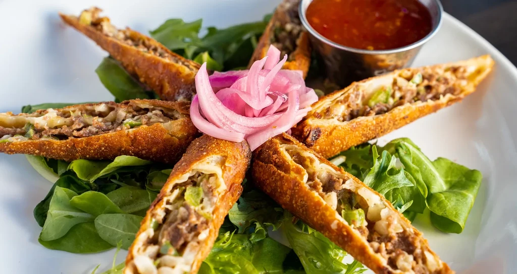 Fried spring rolls with meat filling, lettuce, pickled onions, and dip.
