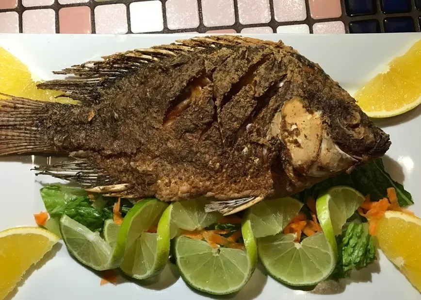 Whole fried fish with limes, lemons, and greens on a plate.