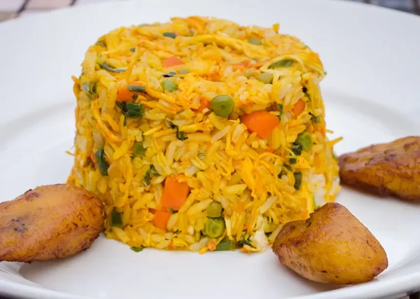 Yellow rice with vegetables and two pieces of fried plantain on a white plate.