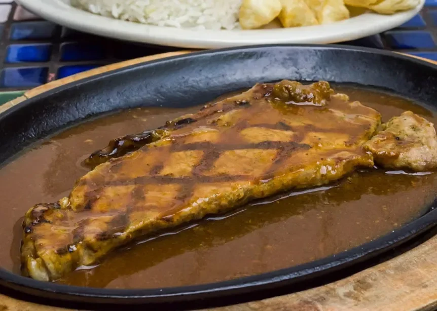 A sizzling skillet of grilled steak in gravy with rice and fries.