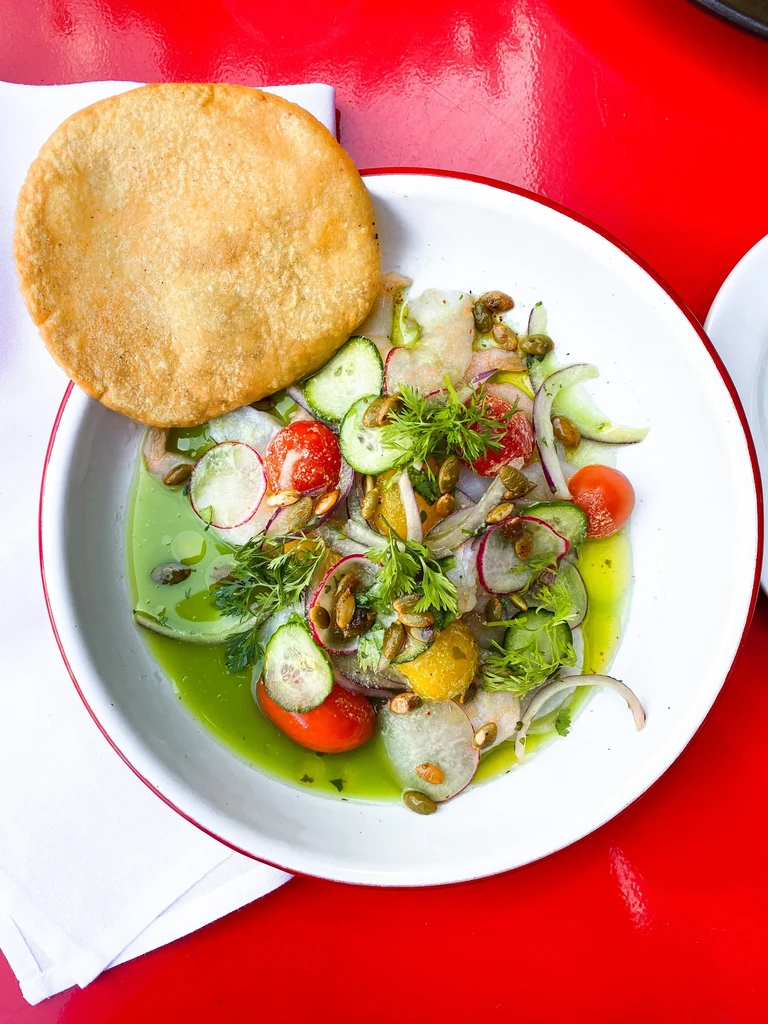 Ceviche in a white bowl with a flatbread on a red table.