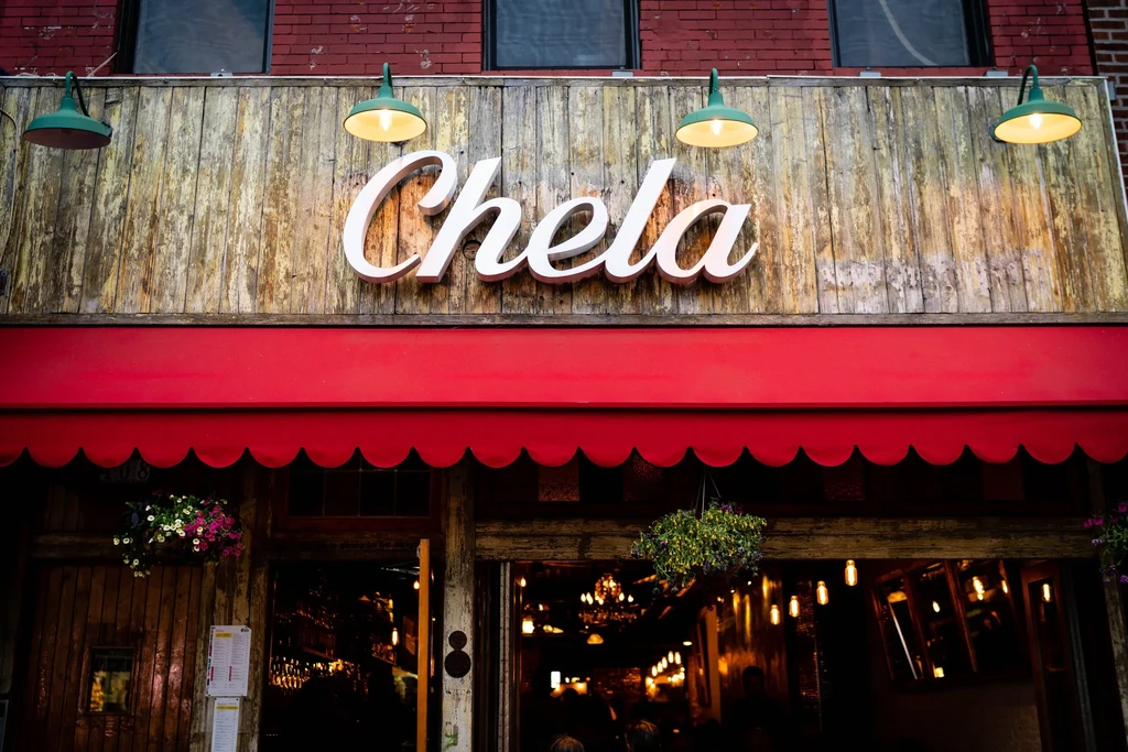 The storefront of Chela restaurant with a red awning.
