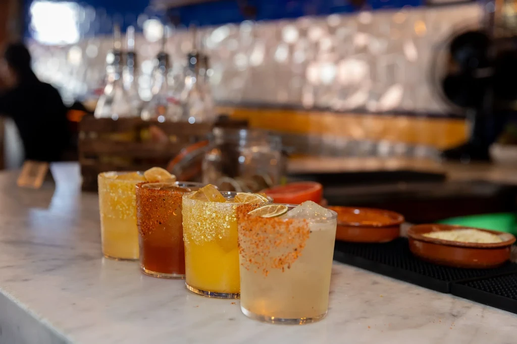 Four cocktails with salt-rimmed glasses on a marble bar.