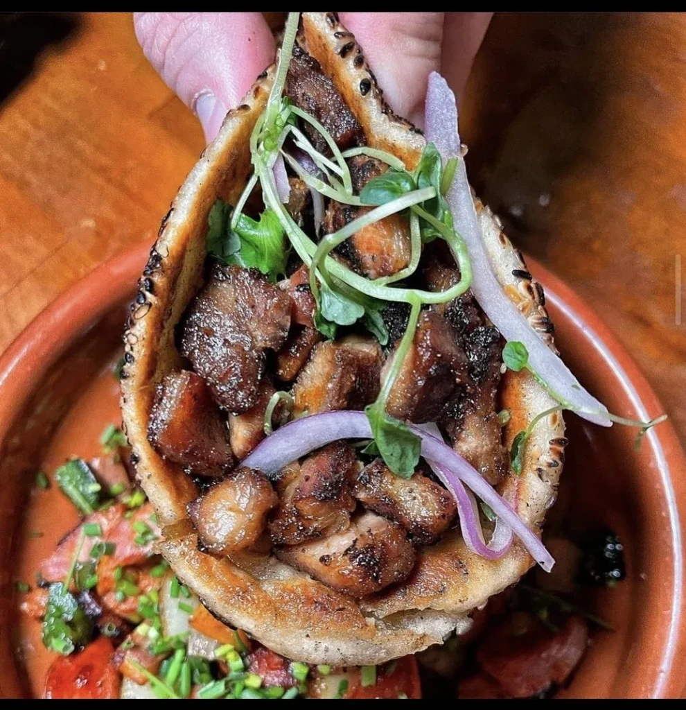 A hand holding a pita filled with meat, onions, and sprouts.