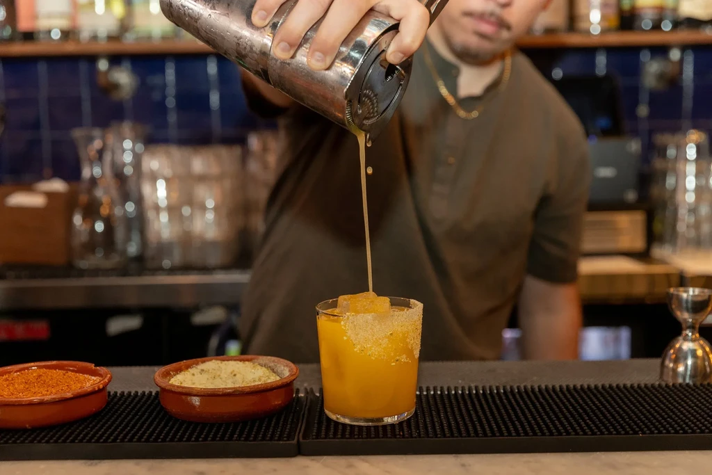 A bartender pours a yellow drink from a shaker into a glass.