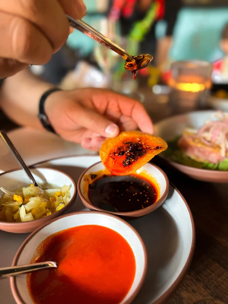 A hand dips a crispy chip into a bowl of chili oil.