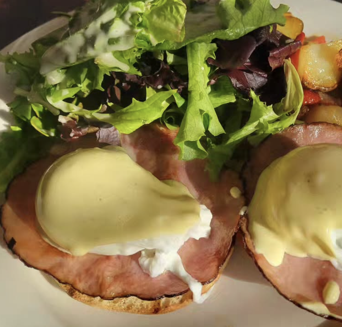 Two eggs benedict with side salad and roasted potatoes on a white plate.