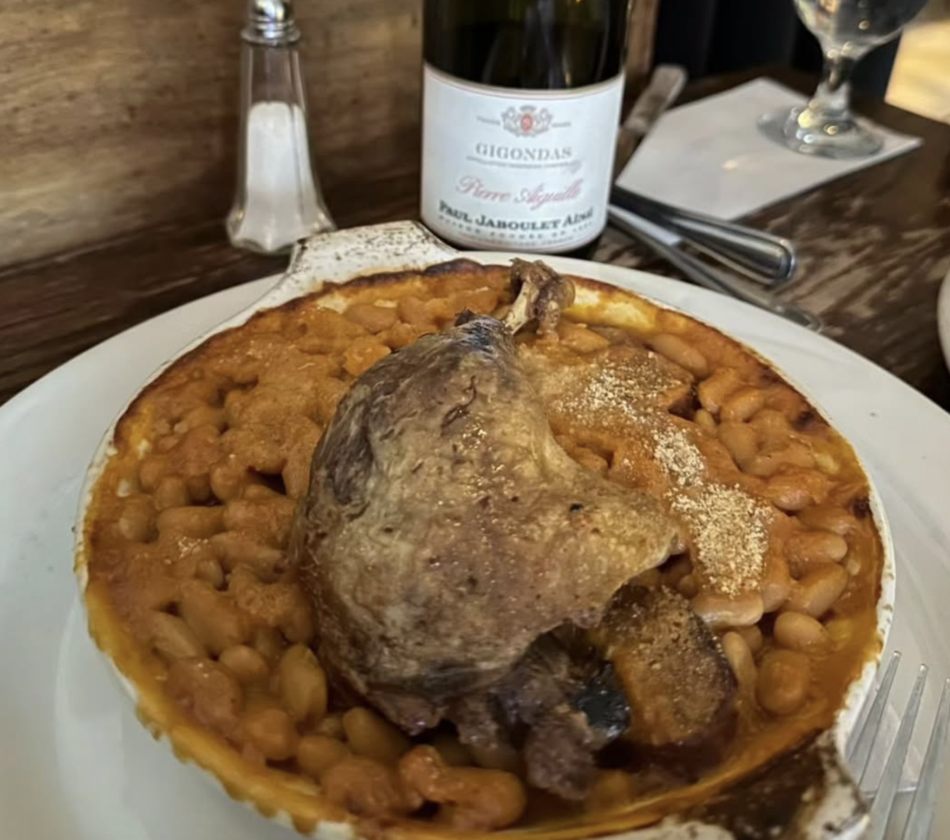 Duck confit cassoulet in an oval dish with a bottle of wine.