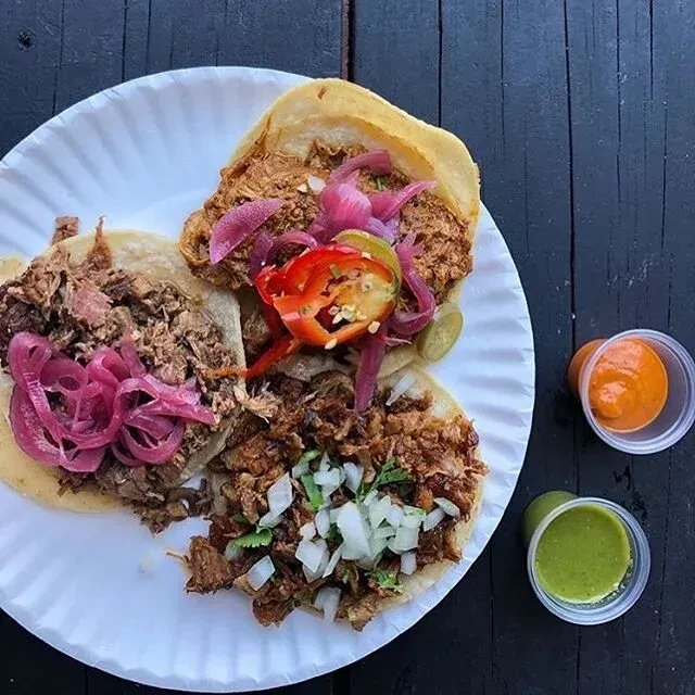 Three meat tacos with toppings on a white paper plate.