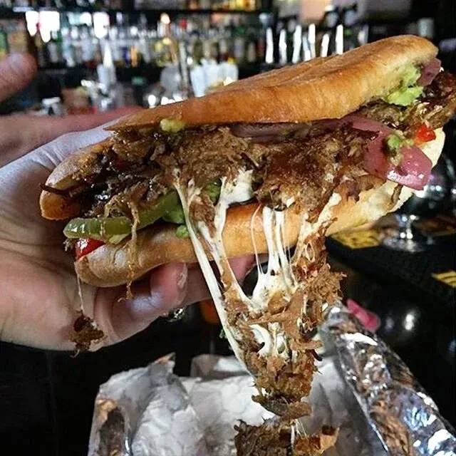 A hand holding a messy sandwich with melting cheese and shredded meat.