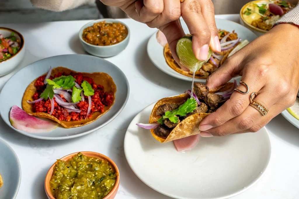 Hands squeeze lime over a taco with meat, onions, and cilantro.