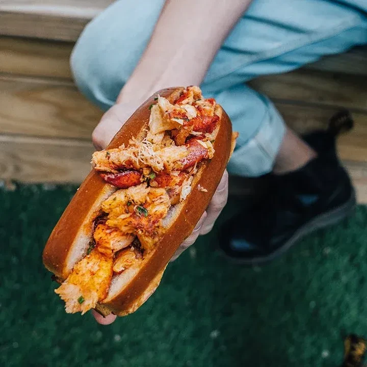 A hand holds a lobster roll overflowing with red lobster meat.