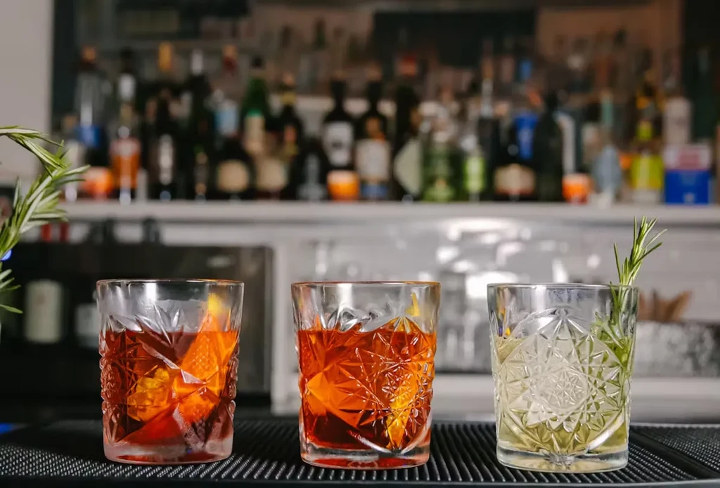 Three cocktails in ornate glasses sit on a bar.