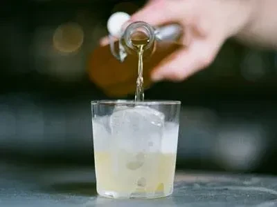 Liquid pours from a bottle into a glass with ice and yellow liquid.