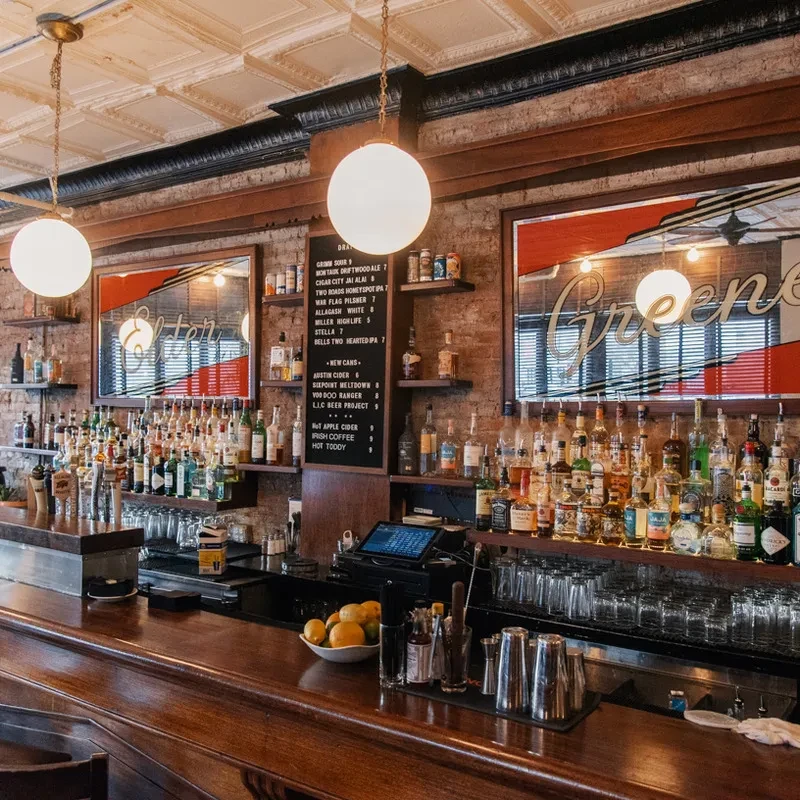 A long, curved wooden bar in a dimly lit brick-walled bar.