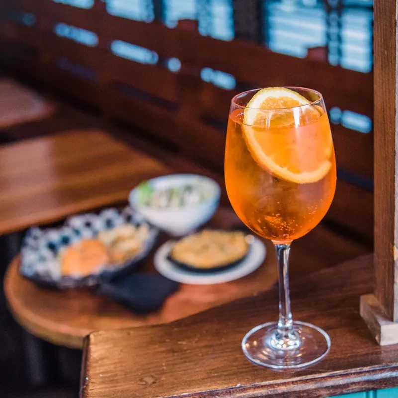 An orange cocktail with a citrus slice and snacks on a wooden table.