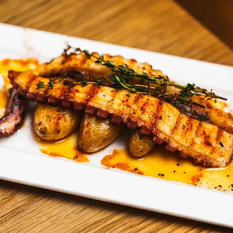 Grilled octopus with small potatoes, drizzled with oil and garnished with herbs.