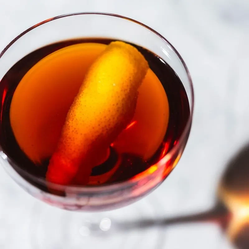 A Negroni cocktail in a glass, garnished with an orange peel.
