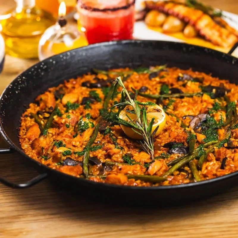 A paella with chicken, green beans, mushrooms, and a lemon wedge.