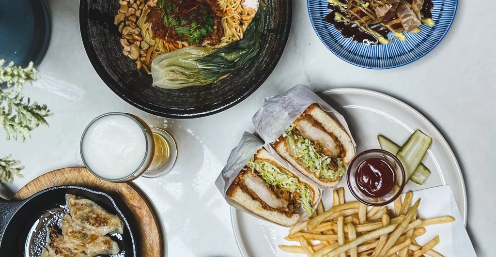Tabletop overhead view of several Asian-inspired dishes and a beer.