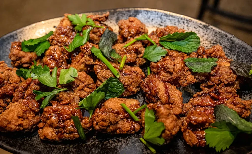 Close-up of crispy fried chicken pieces with sauce and fresh herbs.