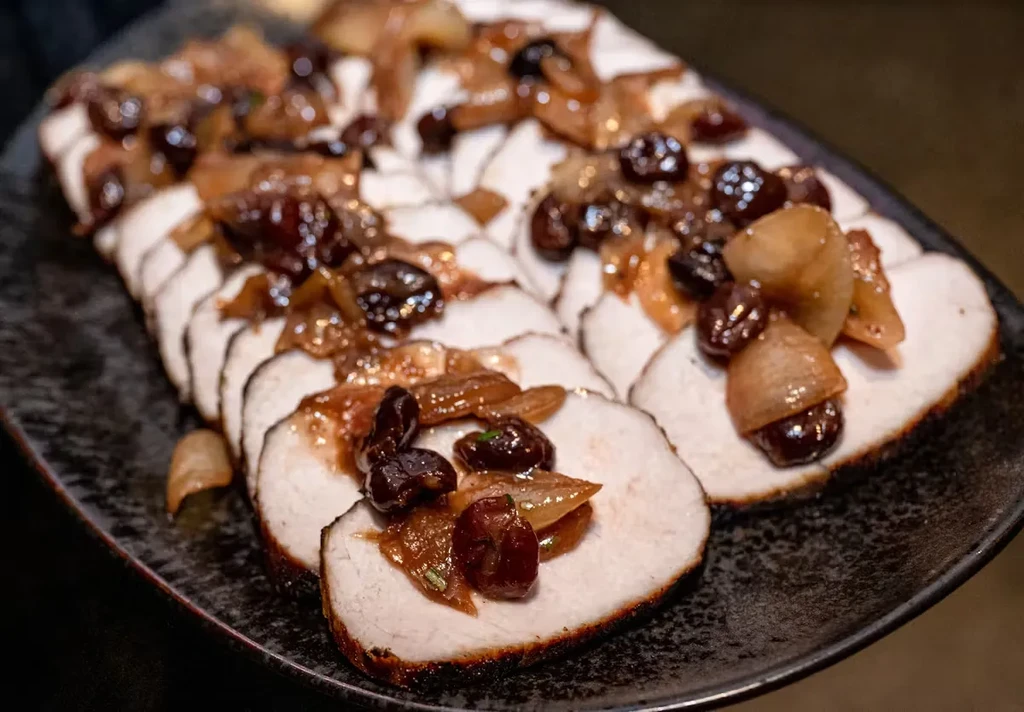 Sliced pork roast topped with caramelized onions and dark berries on a plate.
