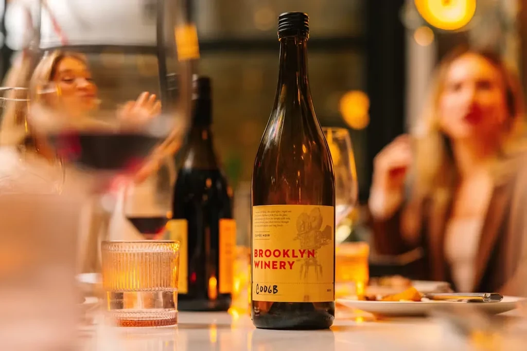 A bottle of Brooklyn Winery wine on a table with blurred people.