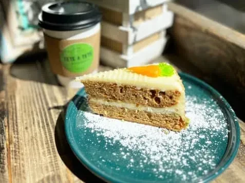 Slice of carrot cake with coffee cup on wooden table.