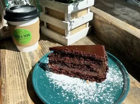 A slice of chocolate cake and a coffee cup on a wooden table.
