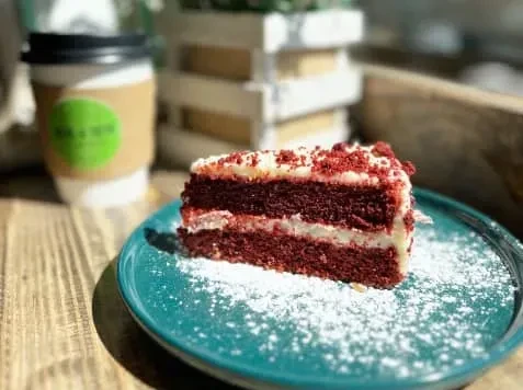 A slice of red velvet cake on a blue plate, with coffee.