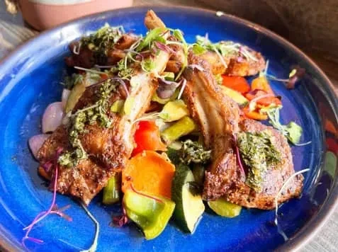 Grilled lamb chops with vegetables and herbs on a blue plate.