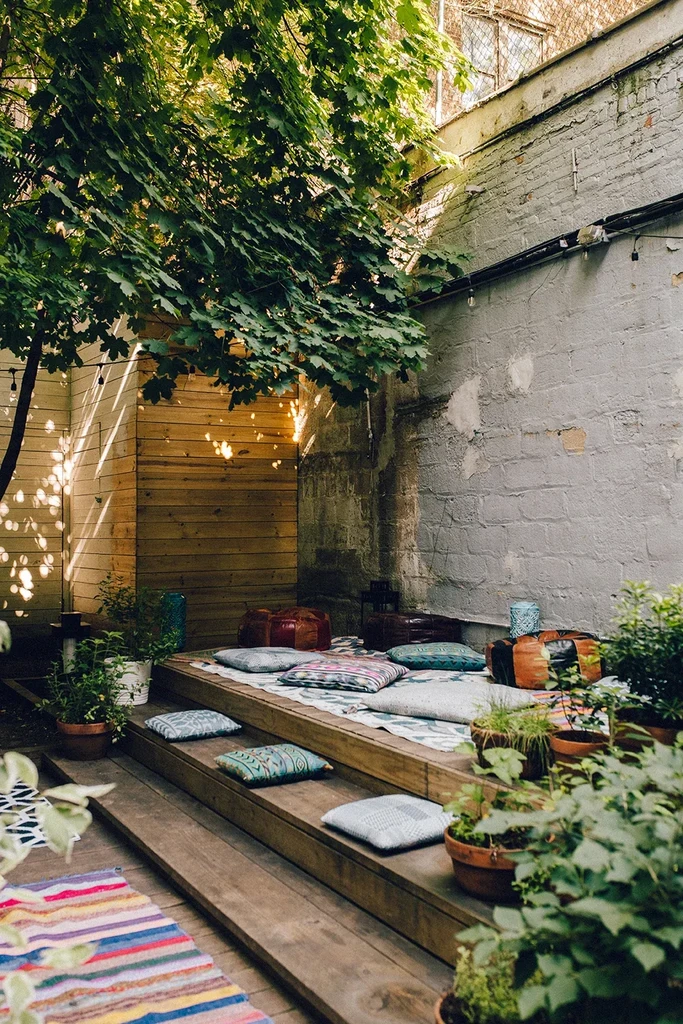 An outdoor patio with wood decking, cushions, plants, and string lights.