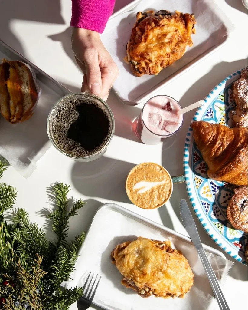 Overhead view of a hand holding coffee surrounded by food and drinks.