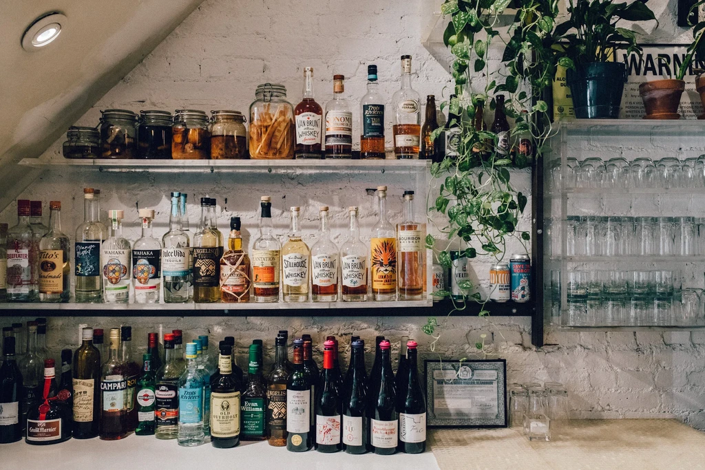 A bar with three shelves of liquor bottles and glasses, against a white brick wall.