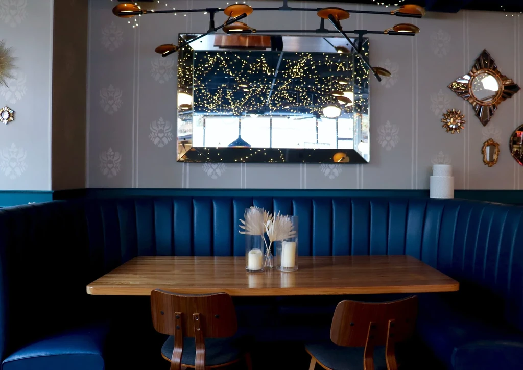 A blue diner booth, wooden table, and wall mirror reflecting lights.