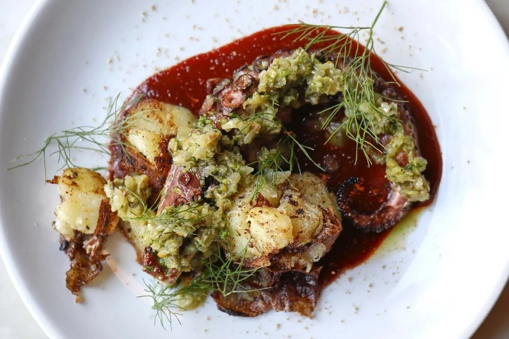 Charred octopus and potatoes with green relish on a white plate.
