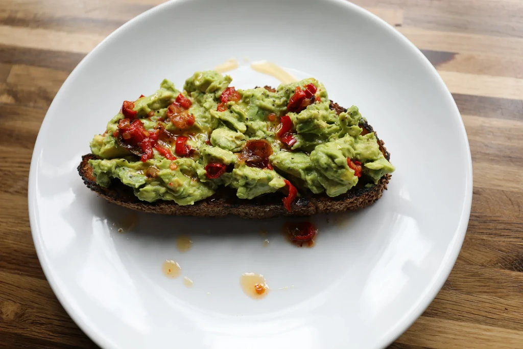 Close-up of avocado toast with red peppers and oil on a white plate.