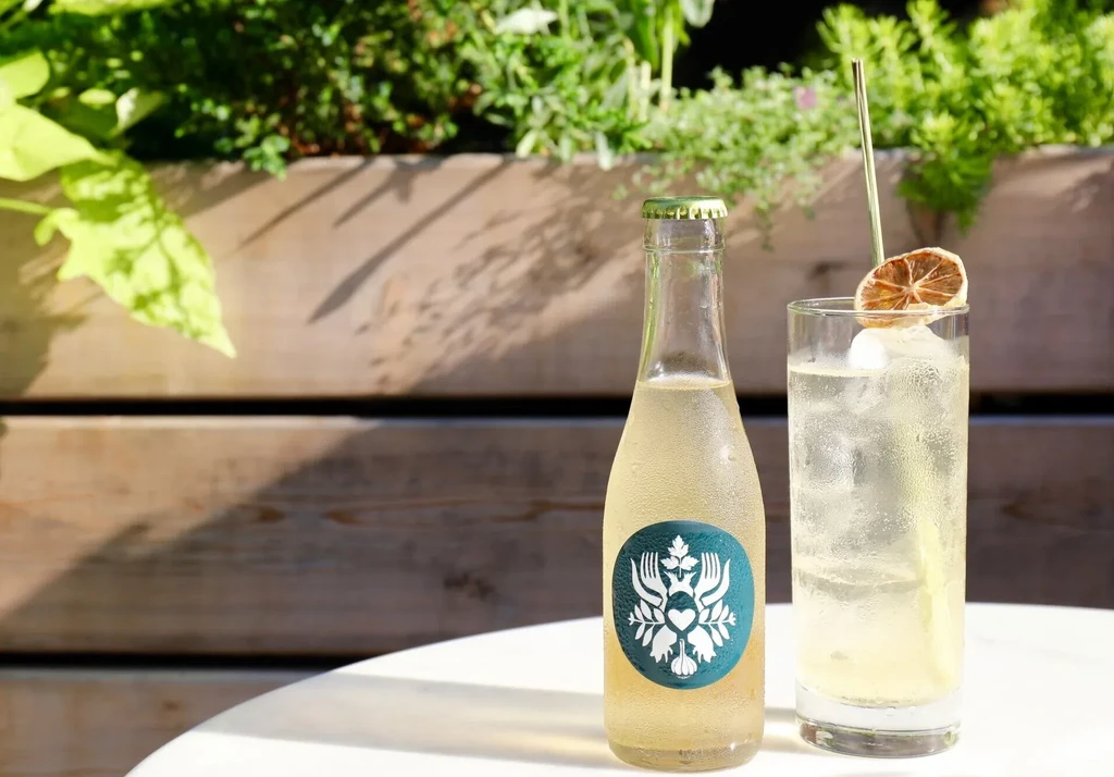 A cold bottle and glass of clear liquid on a white table.