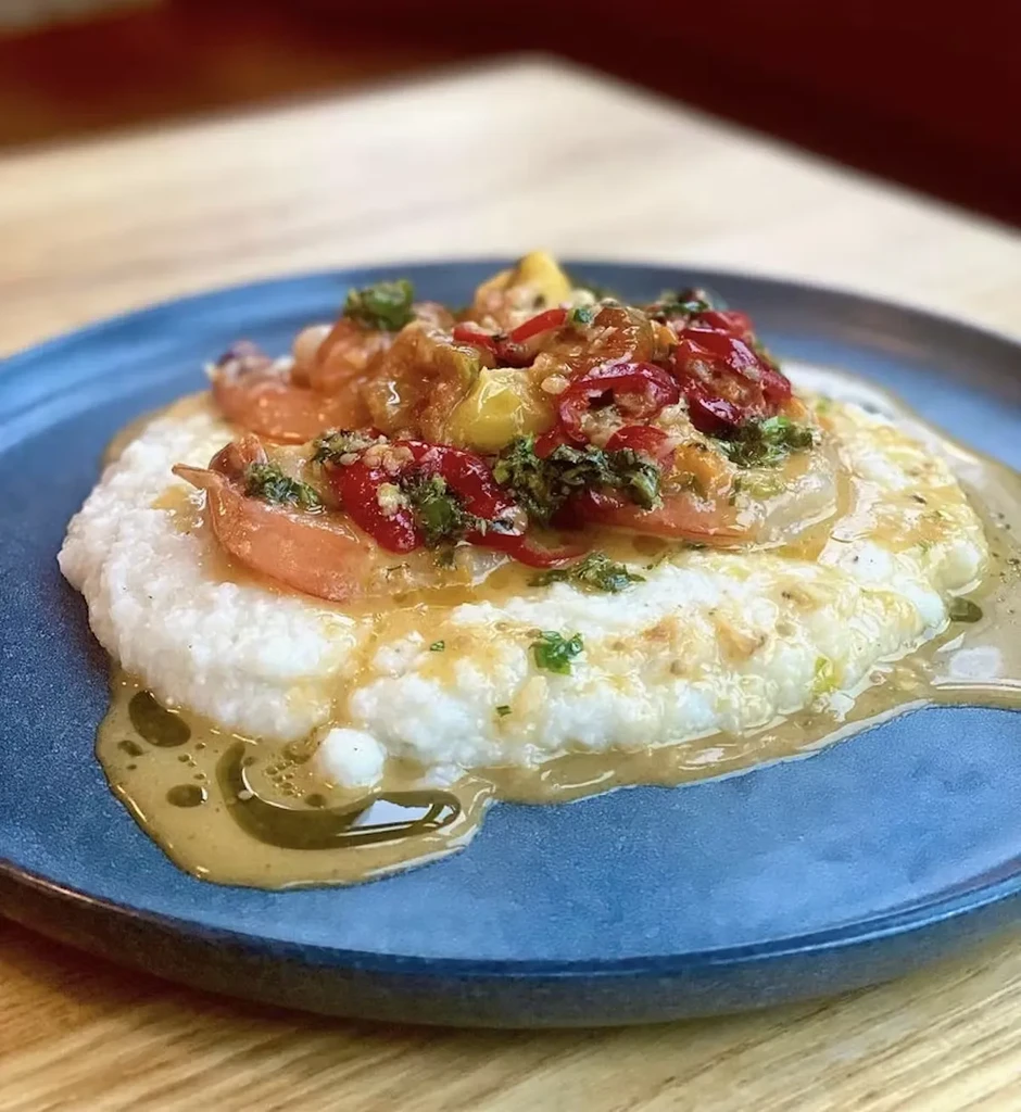 Shrimp and grits with peppers, herbs, and sauce on a blue plate.