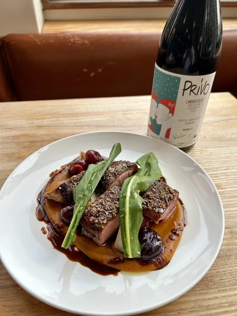 Duck breast, cherries, and arugula on a plate with red wine.
