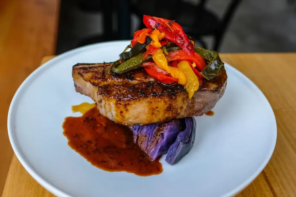 Pork chop with red cabbage and roasted peppers on a white plate.