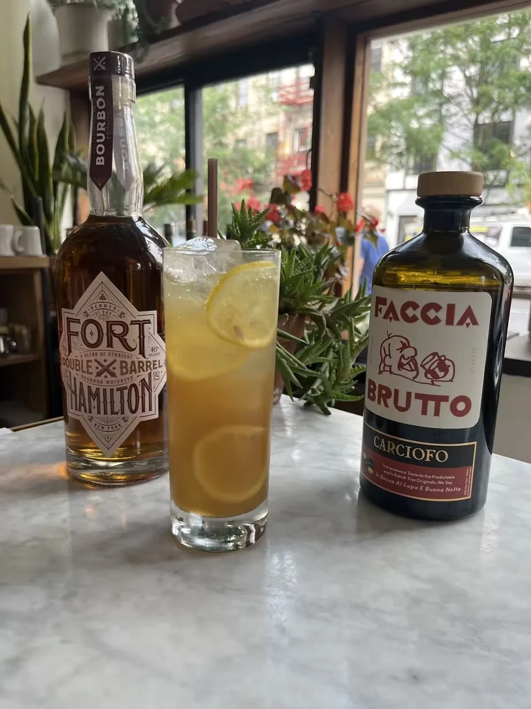 A bourbon bottle, a cocktail, and an amaro bottle on a marble table.