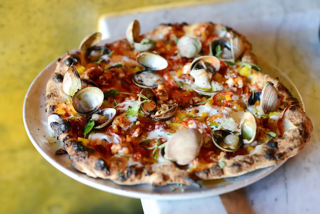 Clam pizza with char marks, tomato sauce, cheese, and herbs.