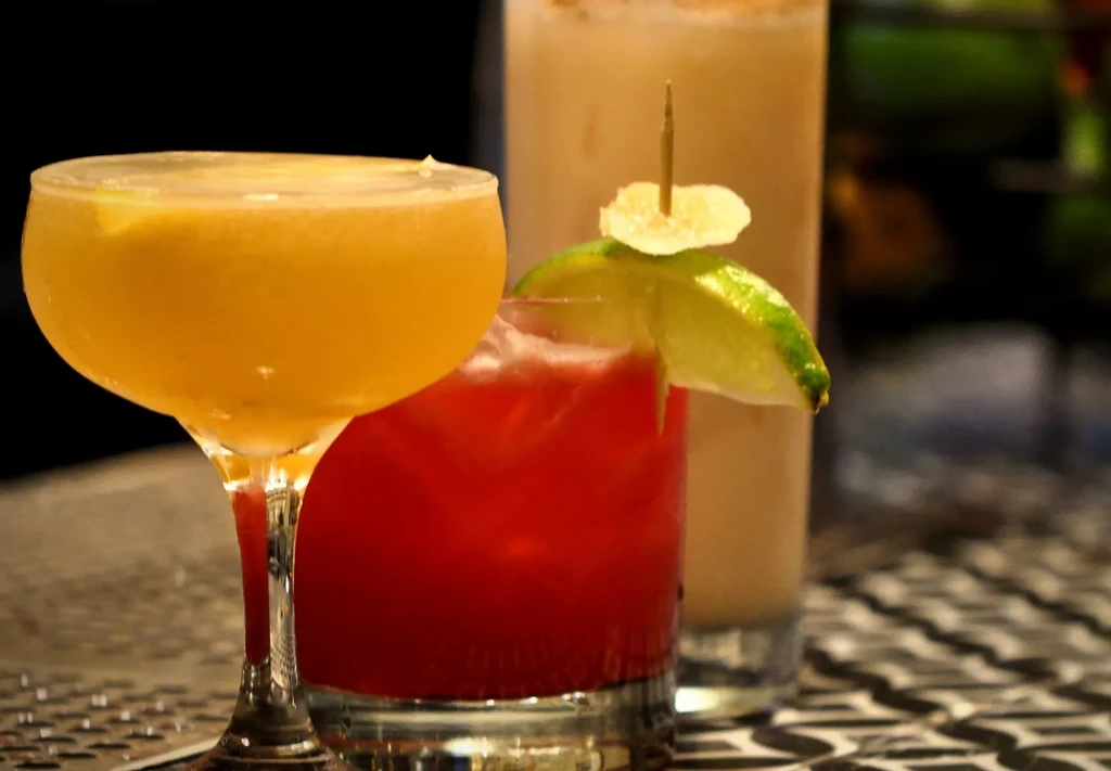 Three colorful cocktails with garnishes on a patterned bar surface.
