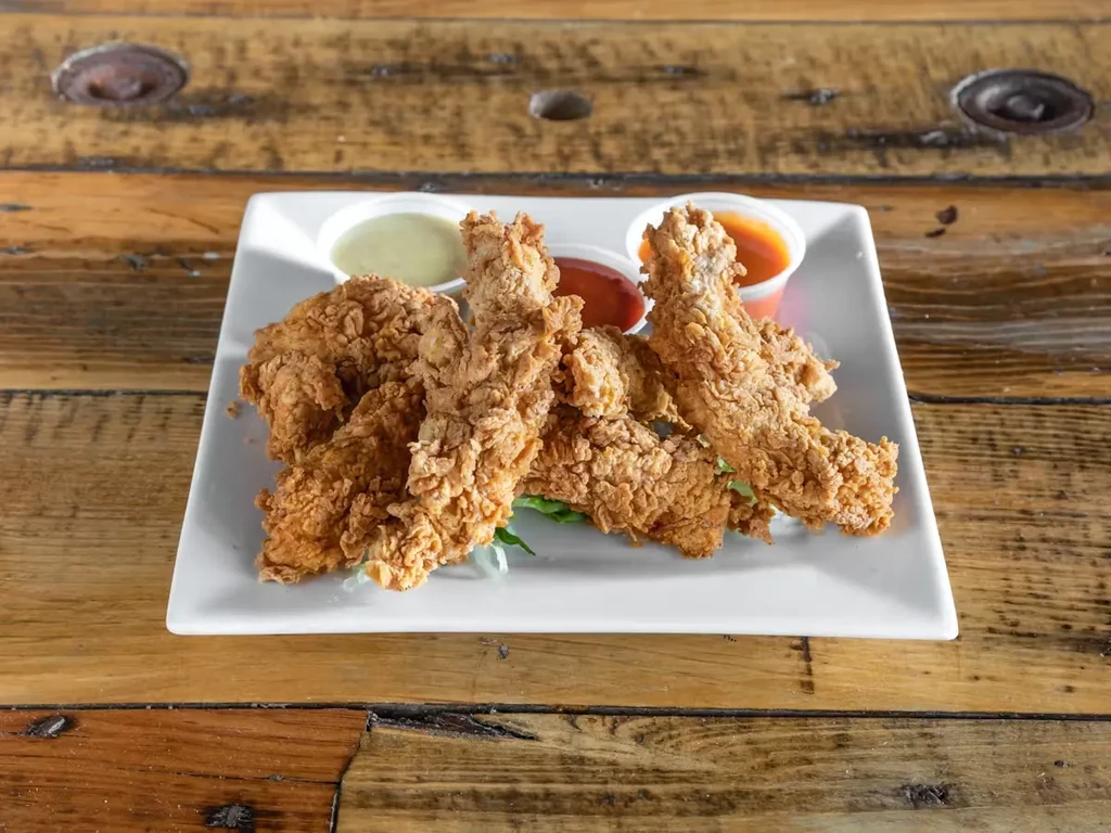 Fried chicken tenders with three dipping sauces on a wooden table.