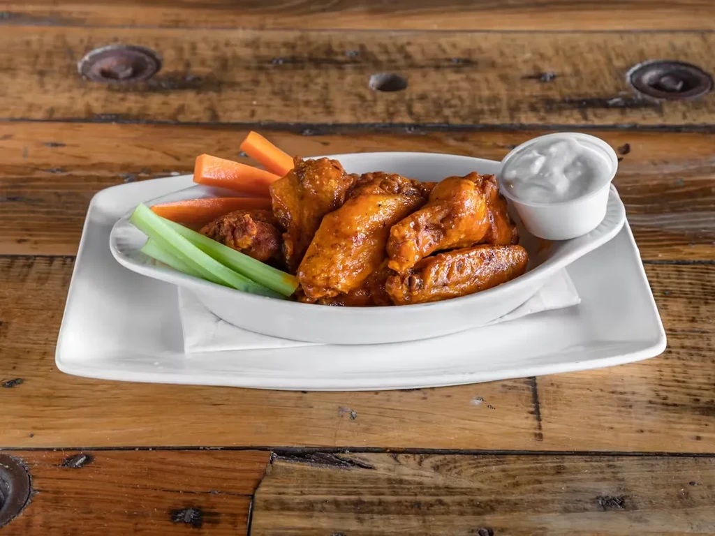 A bowl of chicken wings with celery, carrots, and ranch dressing.