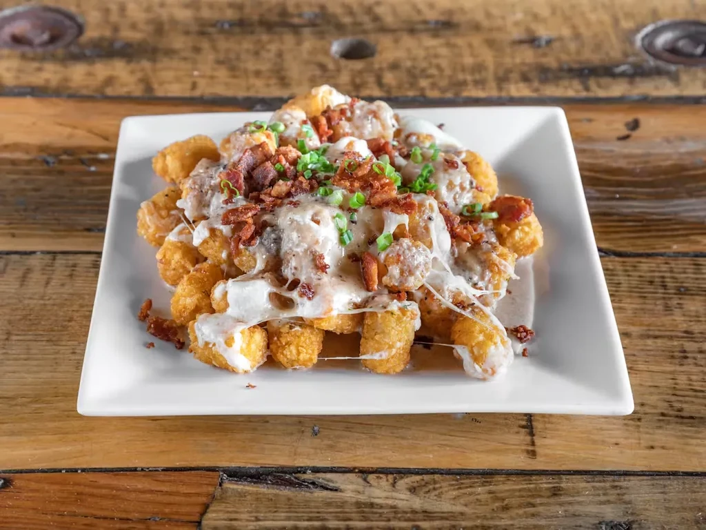 A white plate of loaded tater tots on a wooden table.